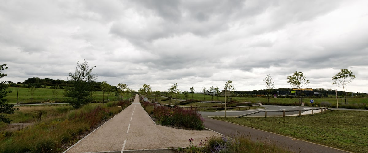 A rural road with a roundabout, surrounded by fields and trees.