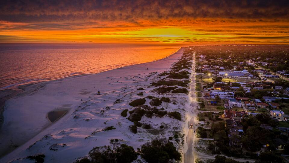 A coastal town at sunset with a beach and houses along the shoreline.