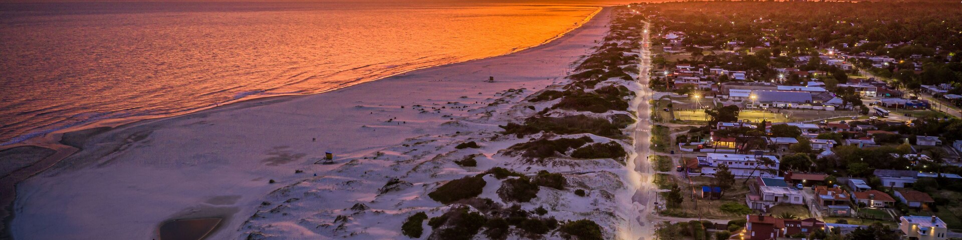 Un pueblo costero al atardecer, con una playa y casas a lo largo de la costa.