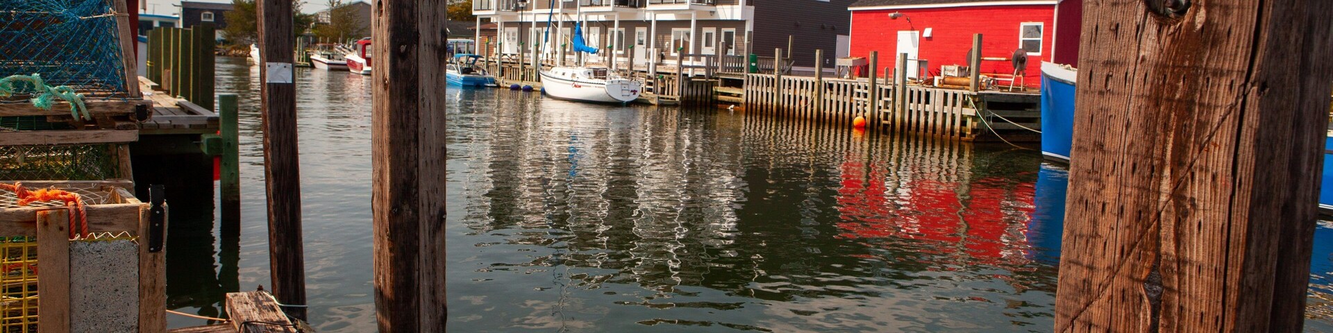 A waterfront with wooden docks, a red building, and a white boat docked near a multi-story building.