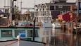 Un puerto deportivo con barcos amarrados, edificios de madera y un edificio rojo al fondo.