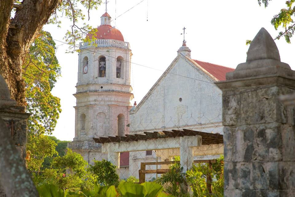 A historic church with a bell tower and a red dome, surrounded by lush greenery.