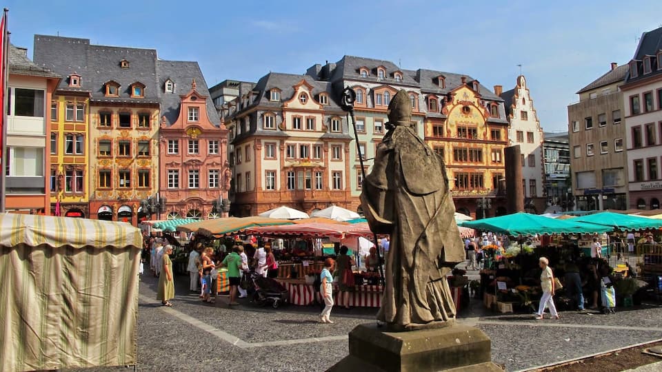 Una animada plaza de mercado con una estatua en primer plano, rodeada de edificios históricos y coloridos.
