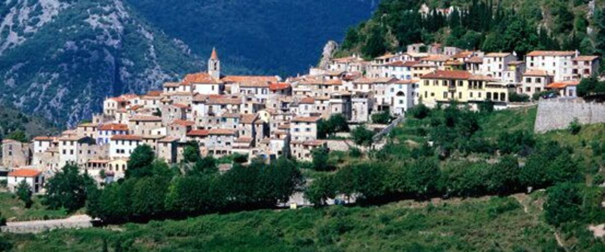 A coastal town with buildings on a hillside, a prominent church tower, and a rocky mountain backdrop.