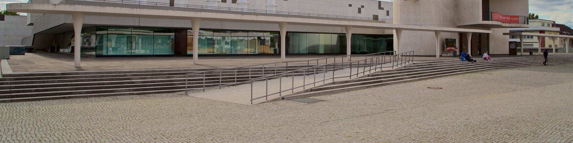 A modern architectural building with a flat roof, large glass windows, and a series of steps leading up to the entrance.
