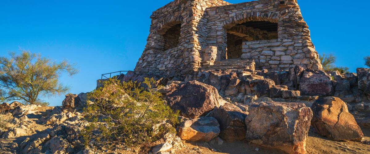 A stone ruin with an arched opening, surrounded by rocks and sparse vegetation.