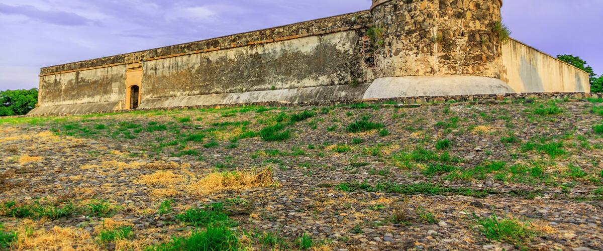 A large, circular fort with a flat roof, surrounded by a grassy hill with sparse vegetation.