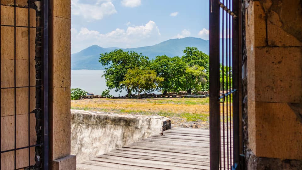 An arched doorway leading to a wooden deck overlooking a lake with mountains in the distance.