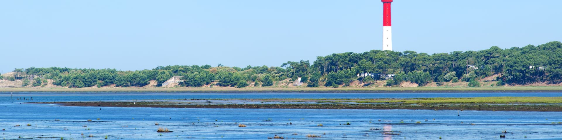 A lighthouse on a small island surrounded by calm water and greenery.