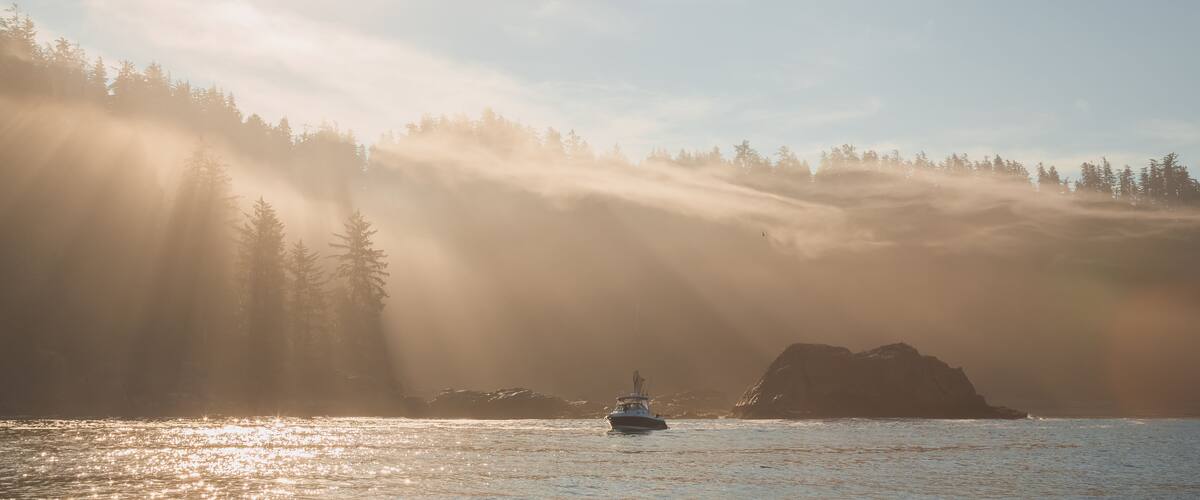 Atmospheric golden light sunbeams through morning mist and fog over an ocean fishing boat off the pacific coast of Vancouver Island near Port Renfrew, BC, Canada.