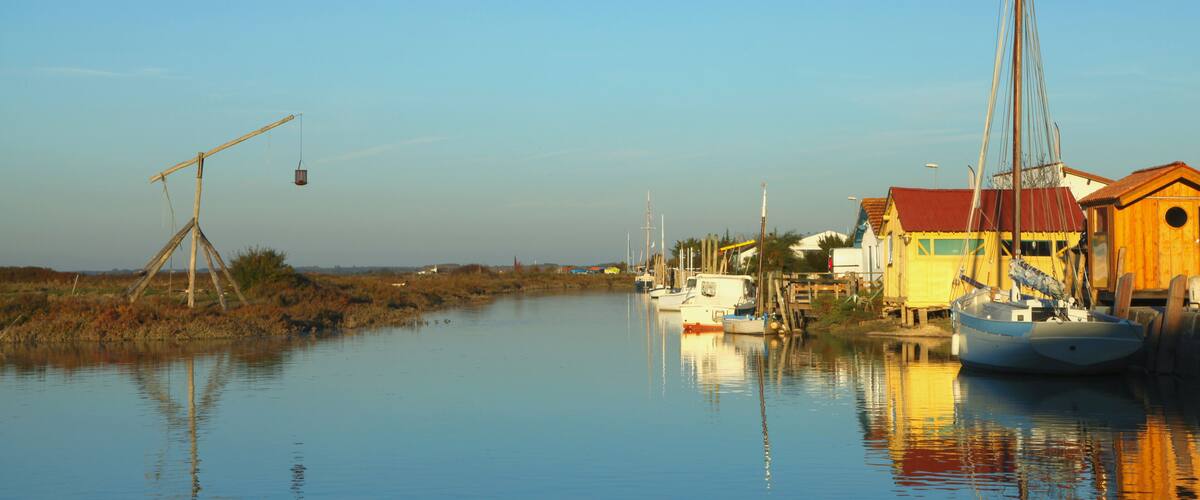 A calm waterway with boats, a wooden structure, and houses with red roofs.