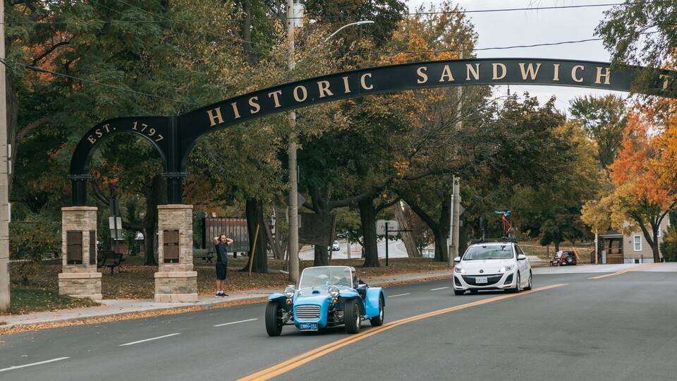 A historic sign arching over a road with vintage cars.