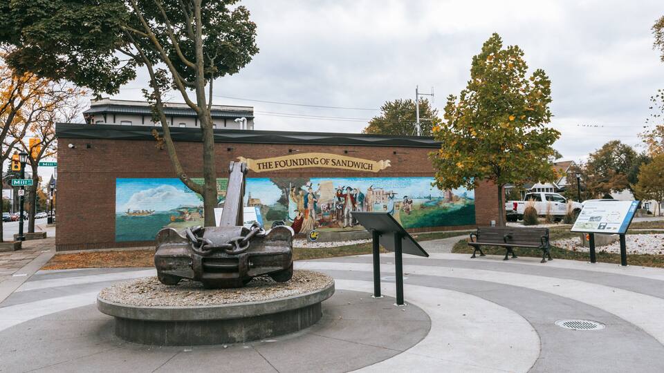A historical mural titled 'The Founding of Sandwich' and a sculpture of a ship's anchor in a park.