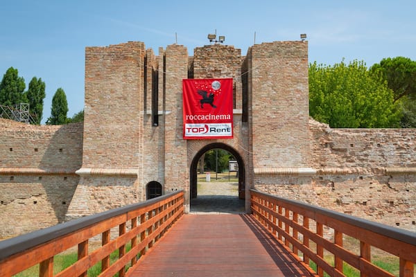 Eine historische Steinbrücke, die zu einem Schloss führt, mit einem roten Banner, das einen Vermietservice bewirbt.