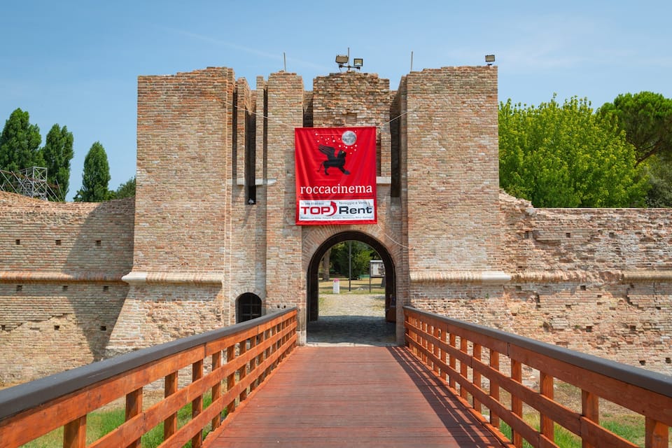 A historic stone bridge leading to a castle entrance with a red banner advertising a rental service.