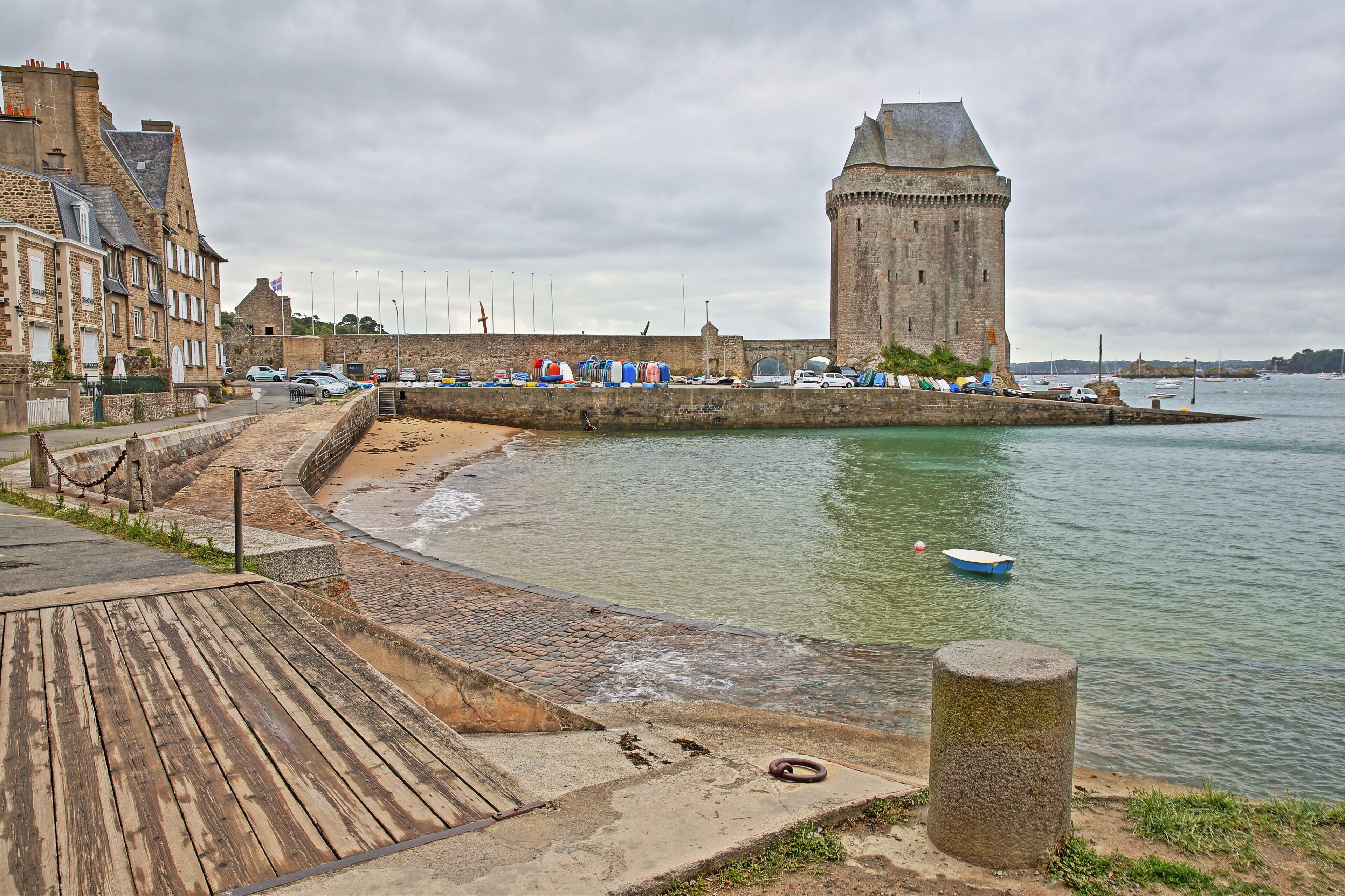 A coastal town with a historic tower, a wooden promenade, and a calm sea.