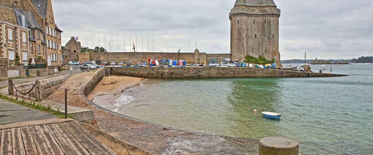 A coastal town with a historic tower, a wooden promenade, and a calm sea.
