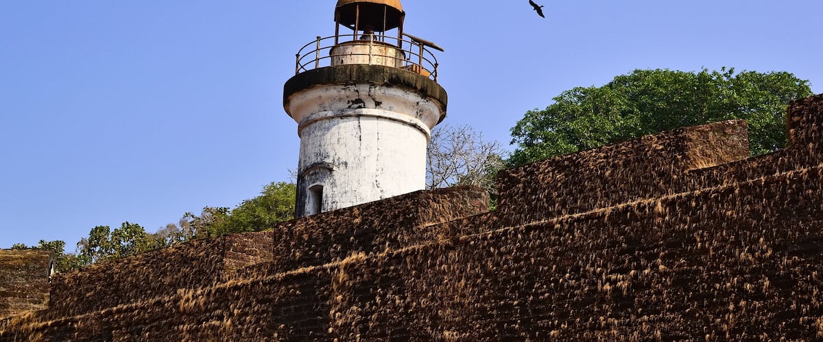 A lighthouse with a domed top and a railing, surrounded by a stone wall and trees.