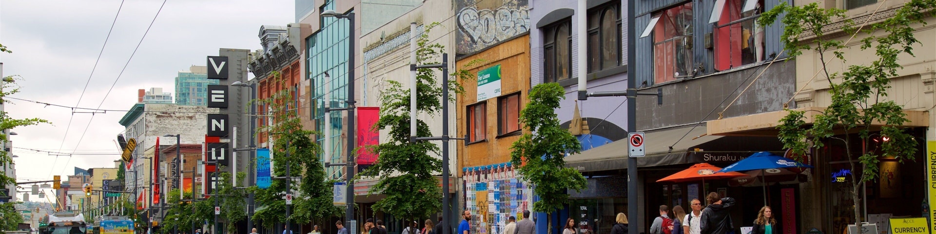 Rua movimentada no centro da cidade, com prédios coloridos, incluindo uma loja 'House of Vintage' e o letreiro 'Venus'.