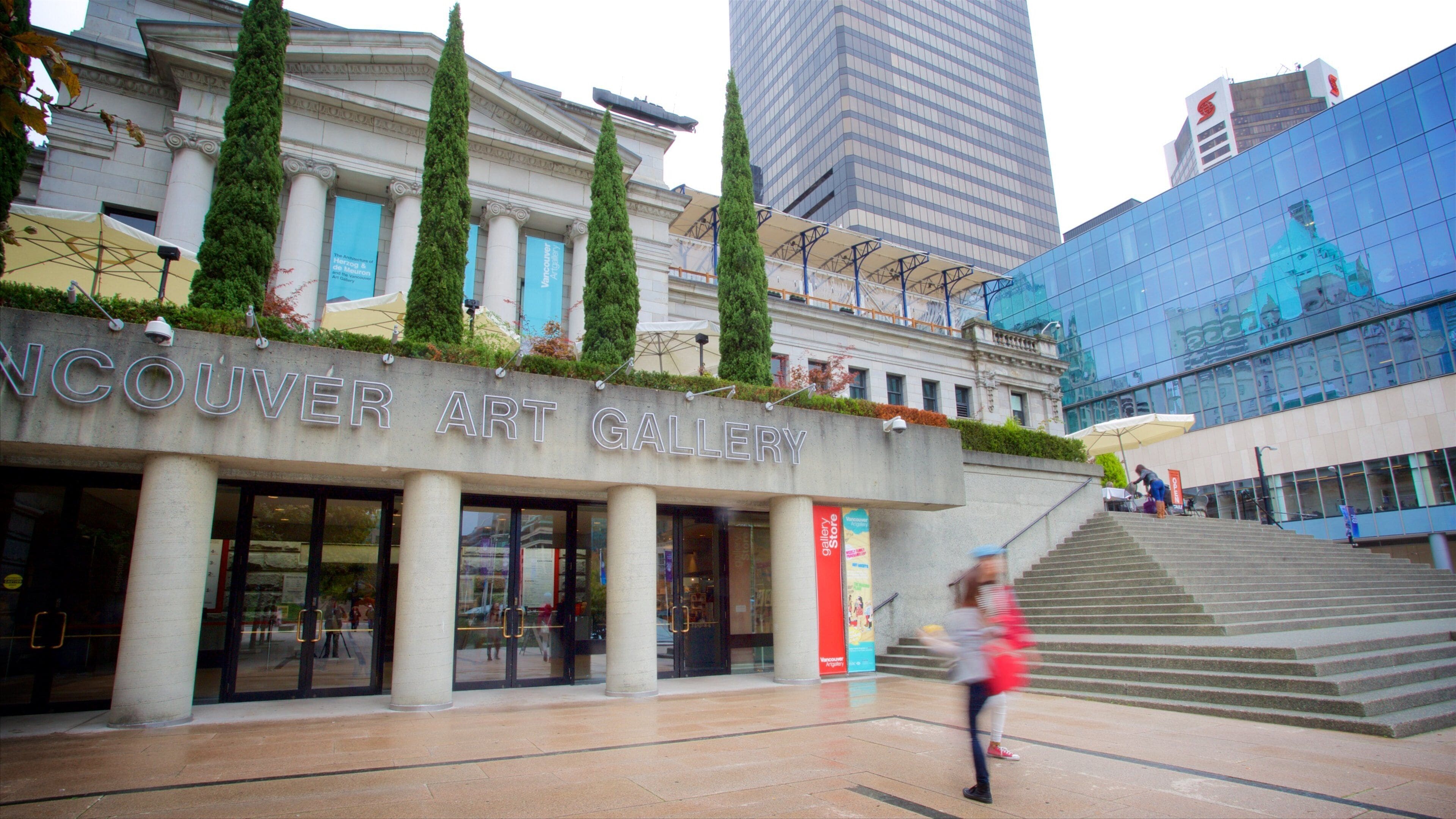 De Vancouver Kunstgalerie met klassieke architectuur, een modern glazen gebouw op de achtergrond, en een persoon die de trap op loopt.