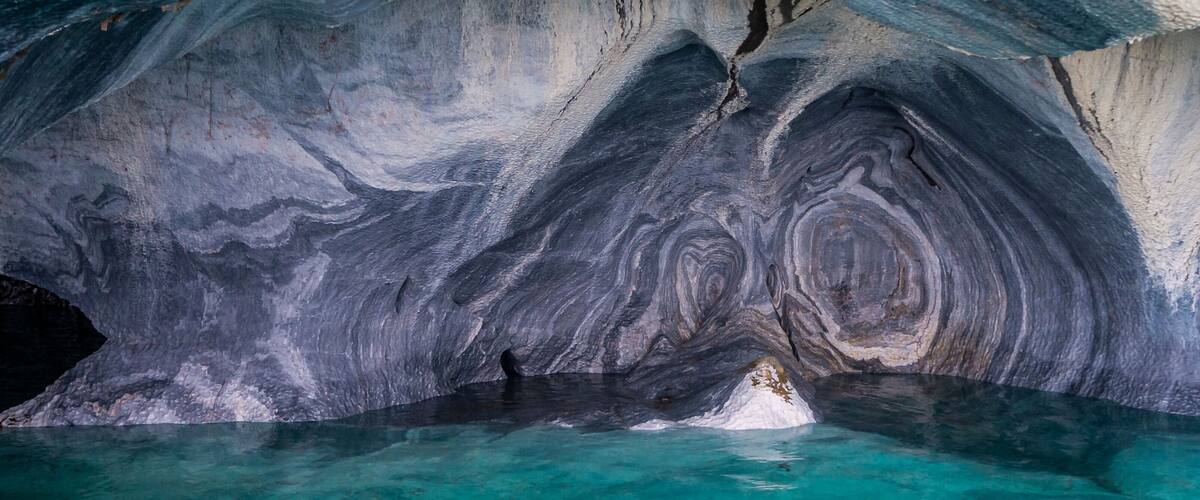 A cave with turquoise water and dark, swirling rock formations.