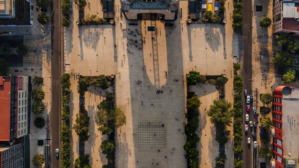 An aerial view of a plaza with a central monument, surrounded by trees and buildings.