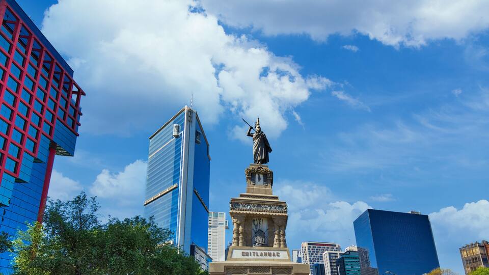 A cityscape with a statue, modern buildings, and a clear blue sky.