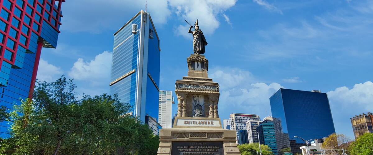 A cityscape with a statue, modern buildings, and a clear blue sky.