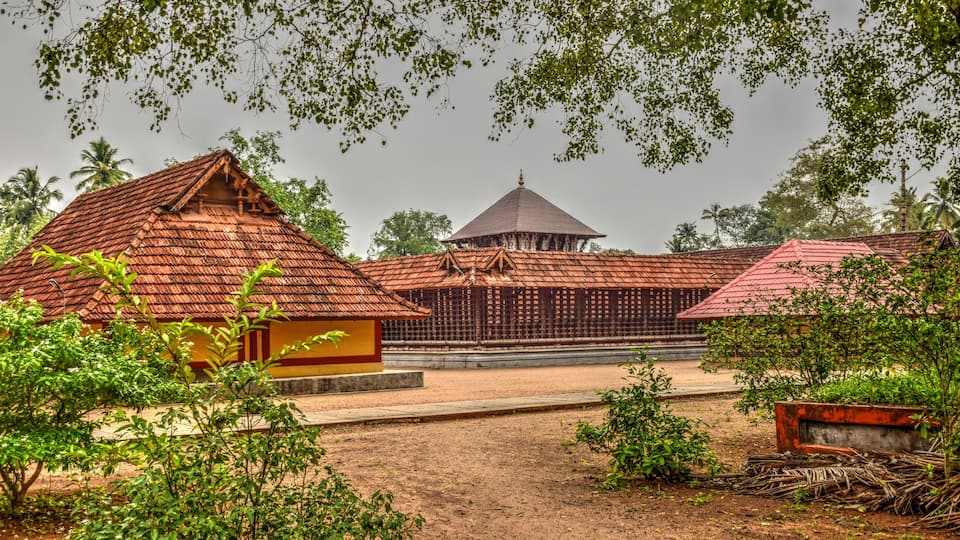 A traditional building with a red roof, surrounded by greenery and palm trees.