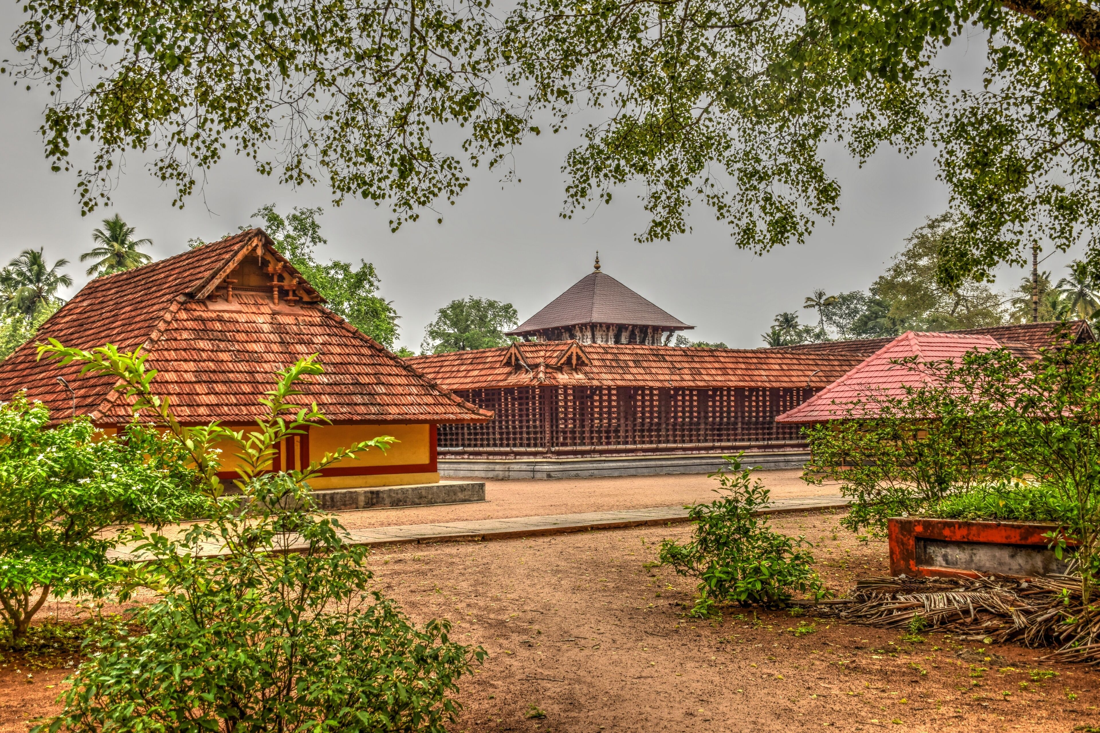 A traditional building with a red roof, surrounded by greenery and palm trees.