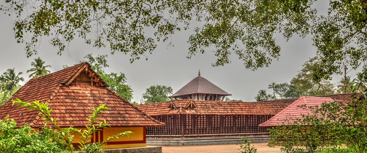 A traditional building with a red roof, surrounded by greenery and palm trees.