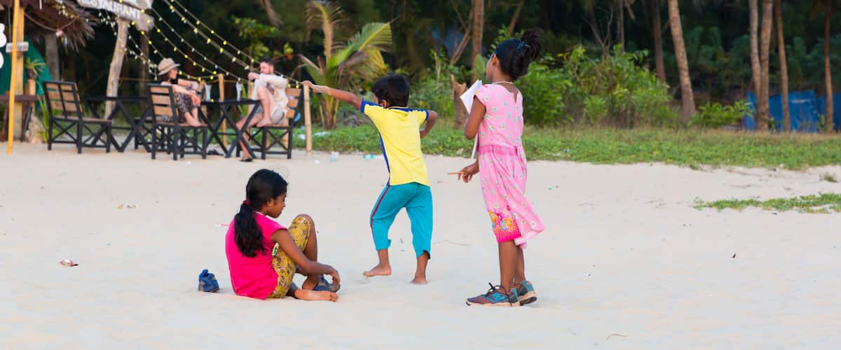 Children playing on a sandy beach with palm trees and a restaurant sign in the background.