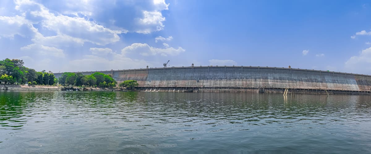 A large dam with a water reservoir, surrounded by greenery and a clear sky.