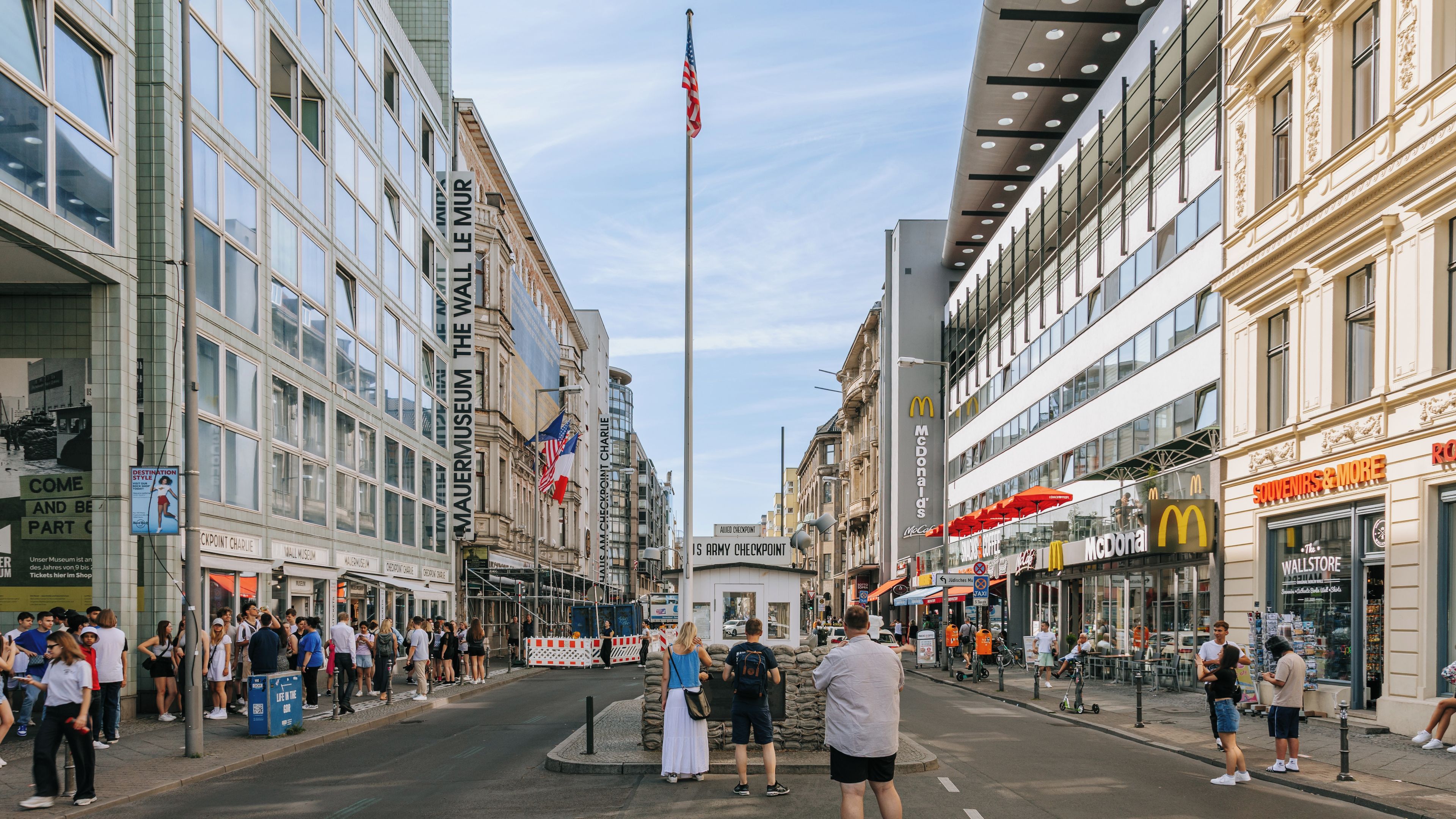 A busy urban street with modern buildings, a flagpole, and various storefronts including a McDonald's.
