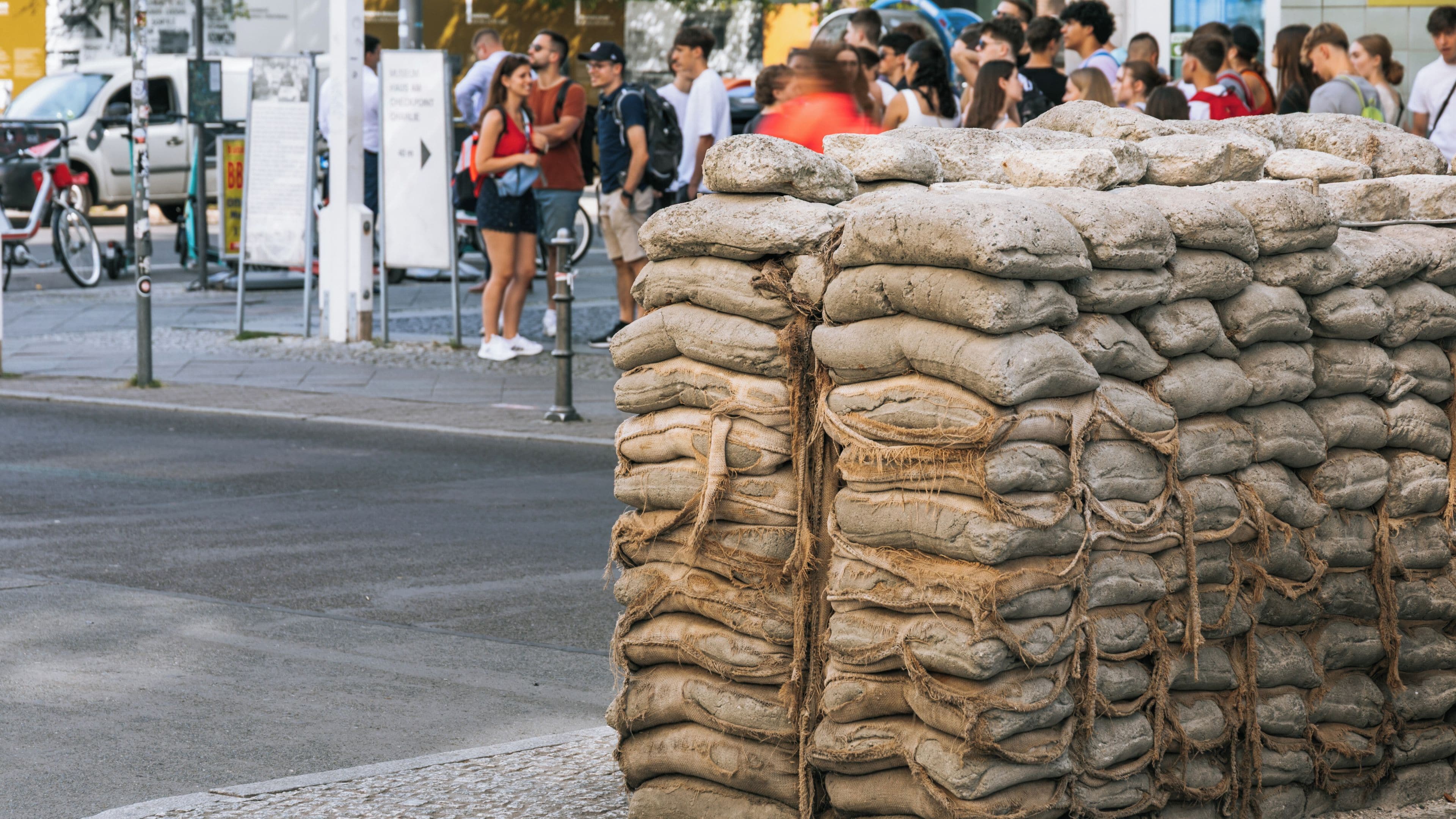 A large stack of sandbags on a street with people in the background.
