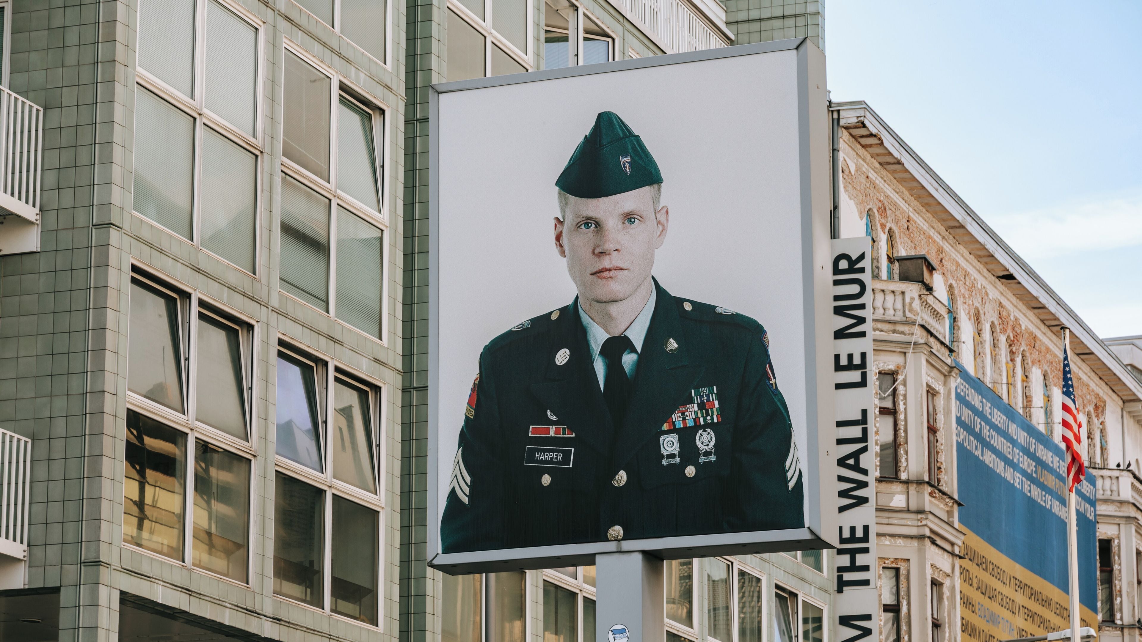 A military portrait on a sign with 'M. THE WALL LE MUR' text.