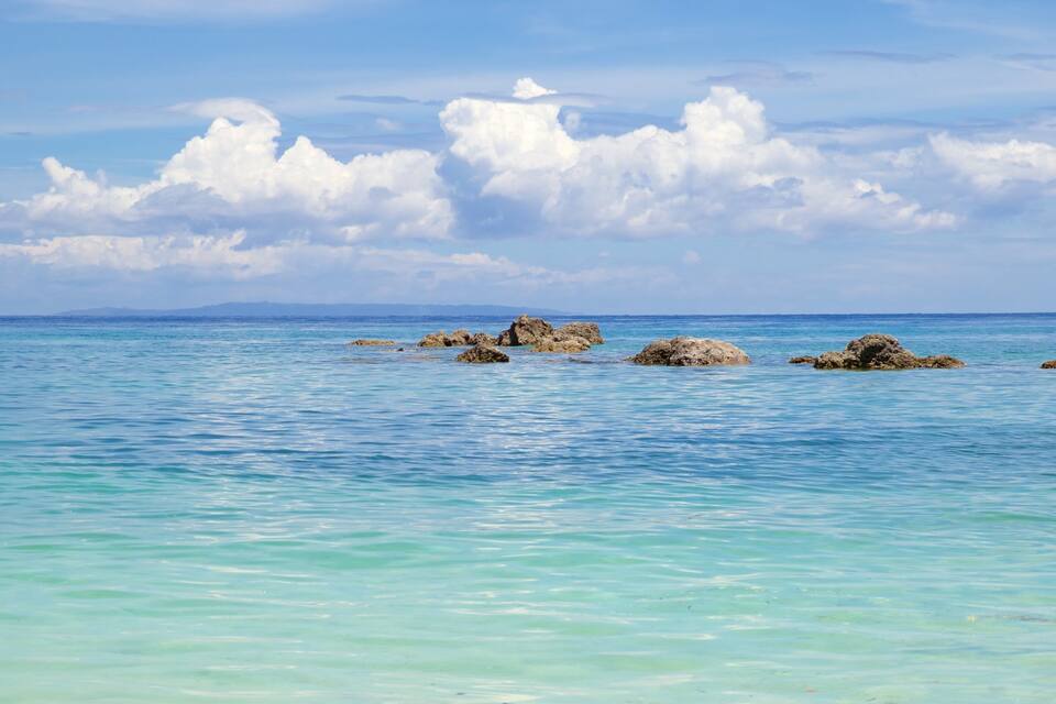 A calm sea with clear turquoise water and scattered rocks.