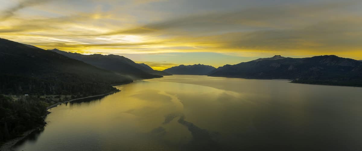 A calm lake surrounded by mountains with a clear sky.