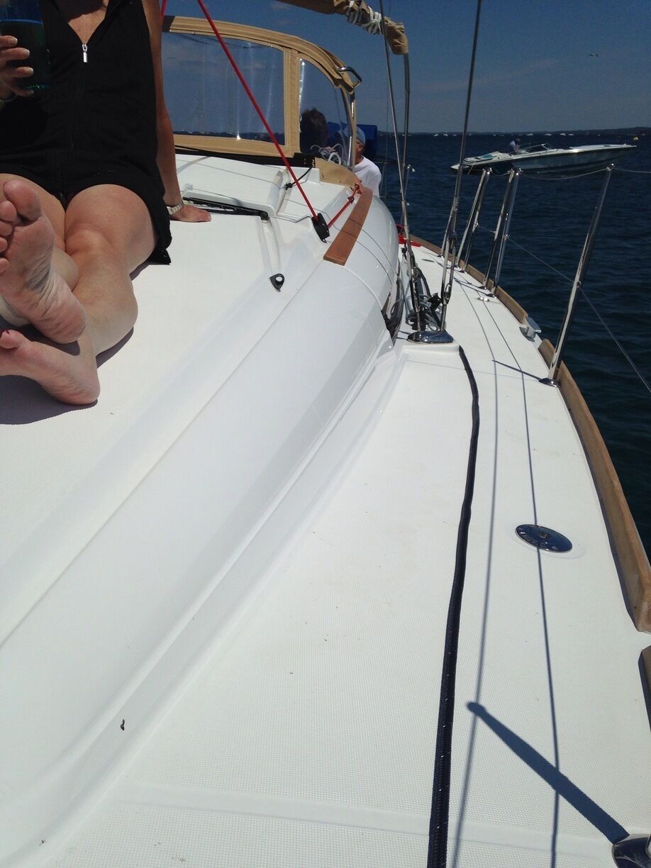 A sailboat's deck with a person sitting, ropes, and a wooden structure.