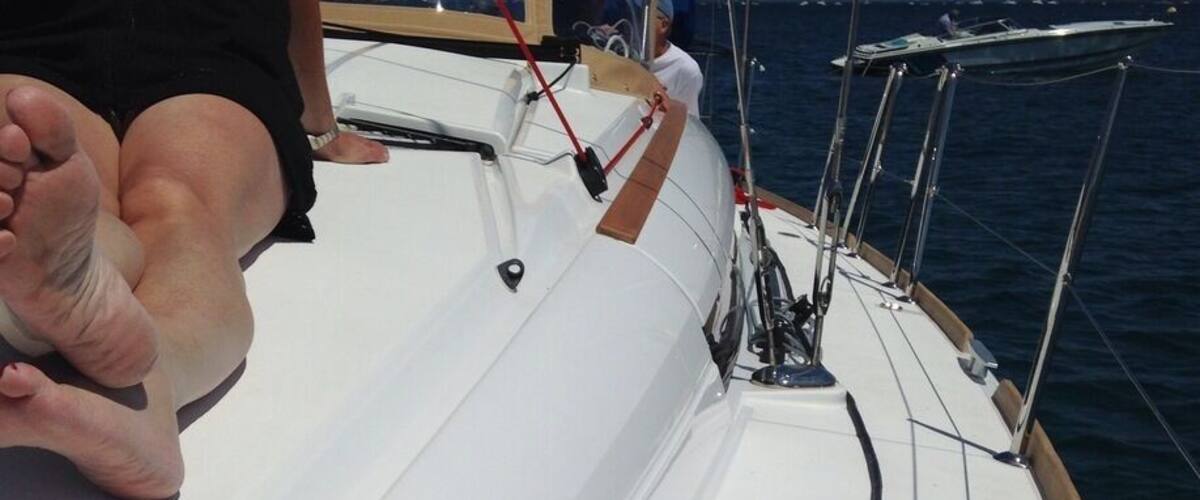 A sailboat's deck with a person sitting, ropes, and a wooden structure.