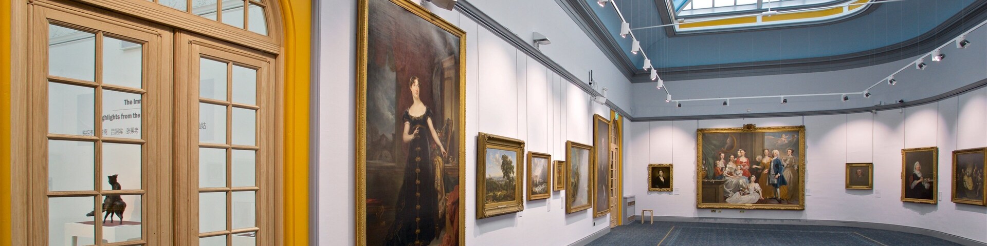 Uma galeria de arte com grandes pinturas nas paredes e uma claraboia acima.