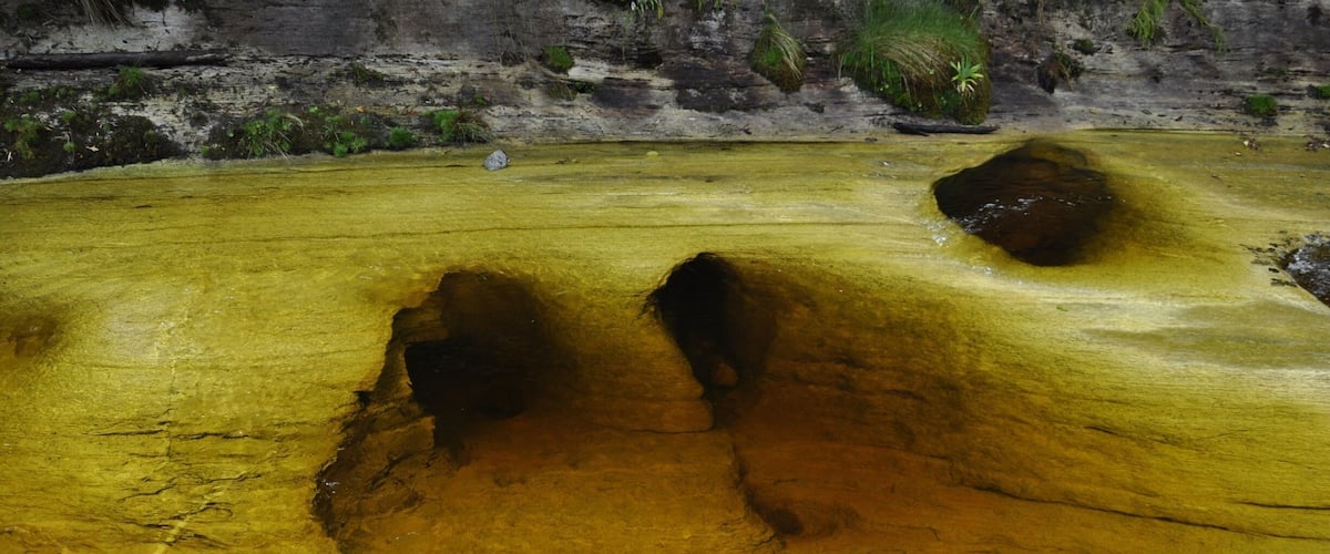 A geothermal pool with yellow and brown water, surrounded by rocky terrain and sparse vegetation.