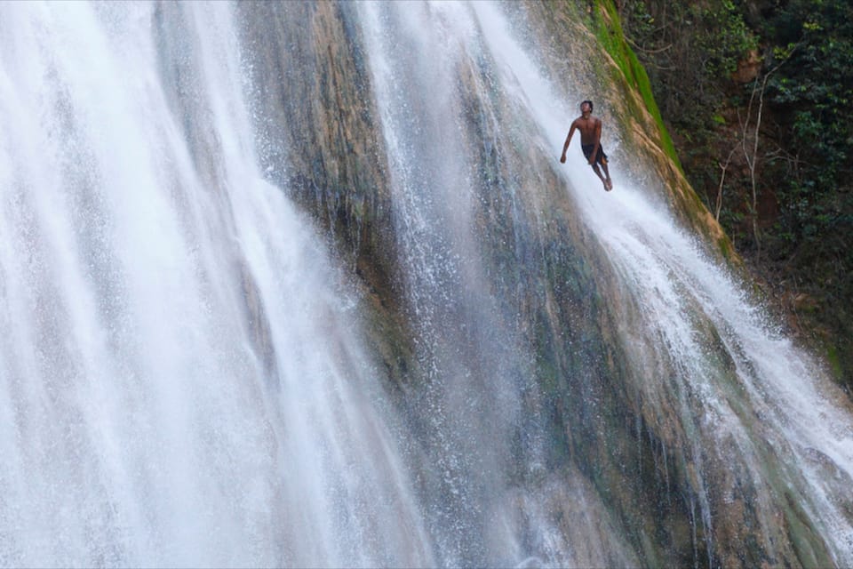 A waterfall with a person jumping off the edge.