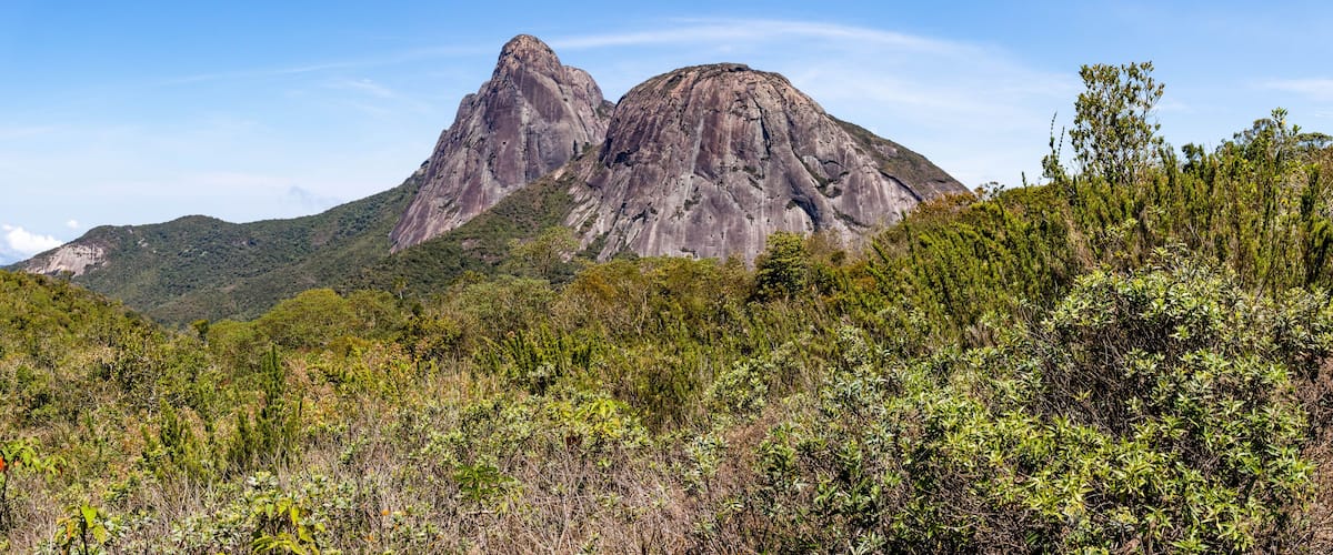 A mountainous landscape with two prominent peaks and dense green vegetation in the foreground.