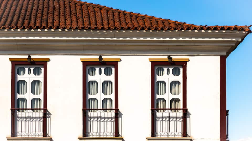 A building with a tiled roof, white walls, and red-framed windows.