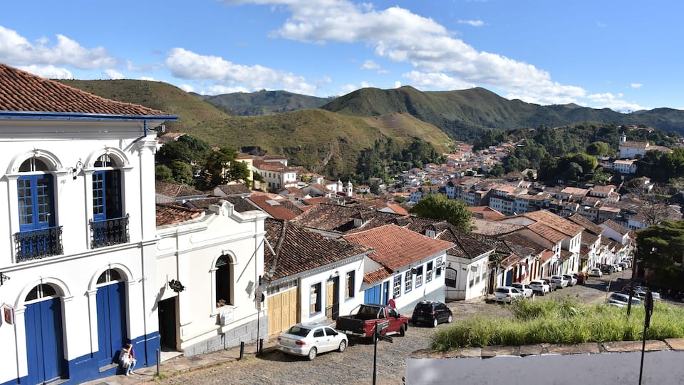 A cobblestone street lined with colorful buildings, a church, and a mountainous backdrop.