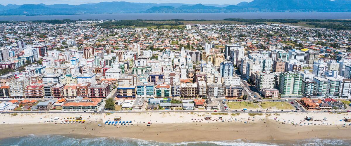 A coastal cityscape with a beach, buildings, and mountains in the background.