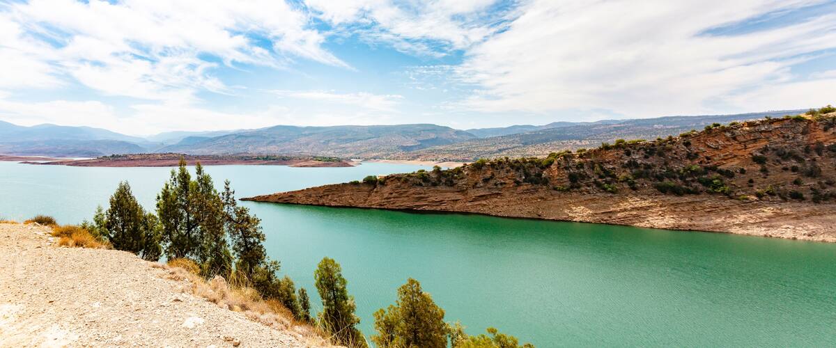 A turquoise lake surrounded by rocky hills and sparse vegetation.