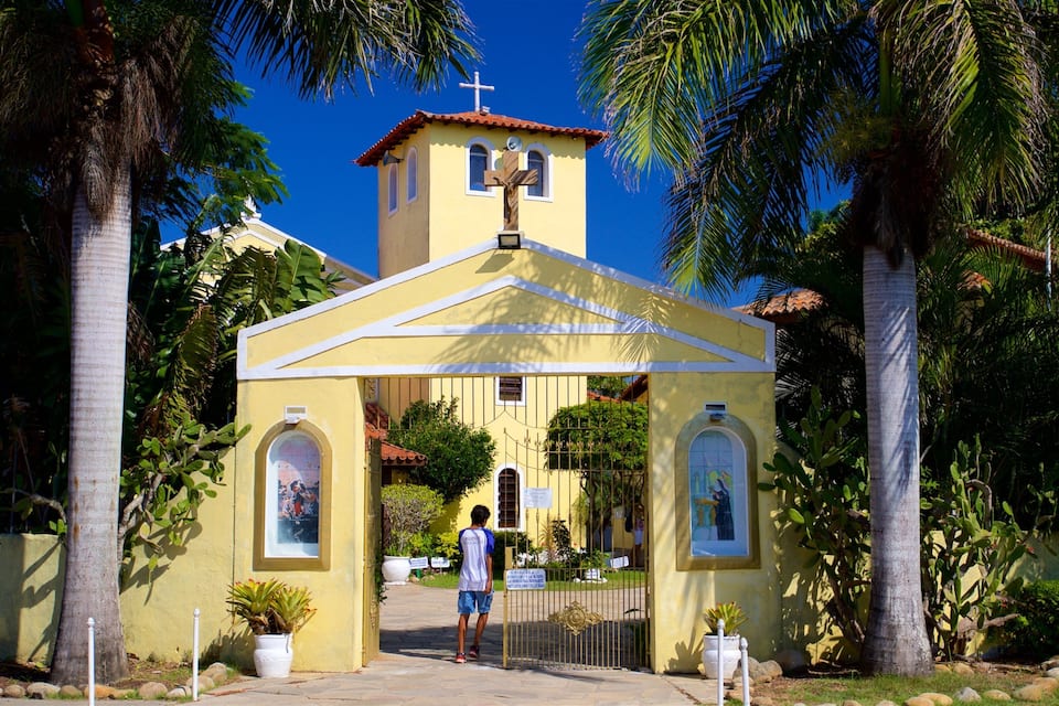 A yellow church with a cross on top, surrounded by palm trees.