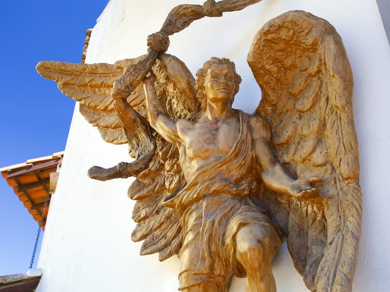 A golden angelic sculpture with wings, attached to a white wall.